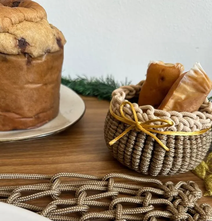 Mini cesto de macramê com laço dourado ao lado do panetone